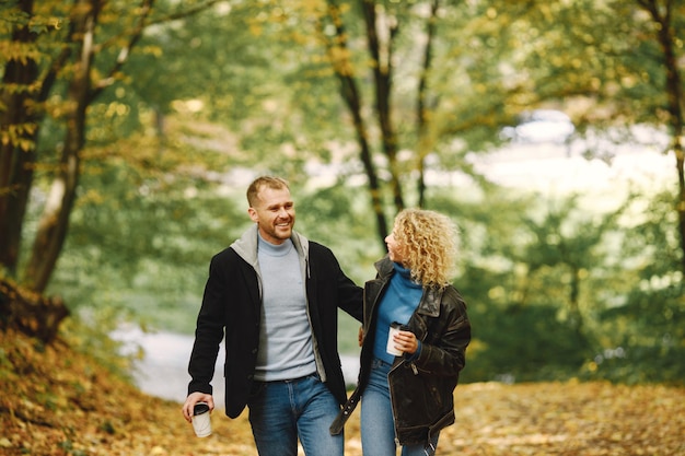 Blonde lockige Frau und Mann, die Händchen halten im Herbstwald und umarmen