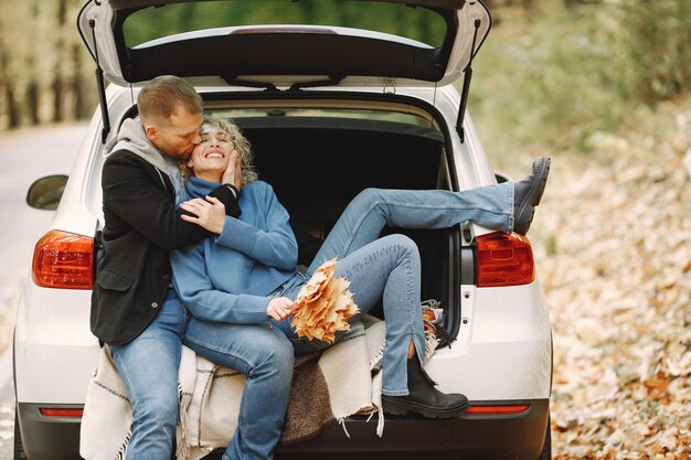 Blonde lockige Frau und Mann sitzen in einem Kofferraum im Auto im Herbstwald und umarmen sich
