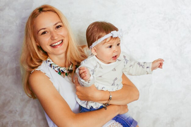 Blonde Mutter hält ihre charmante kleine Tochter mit weißem Bogen