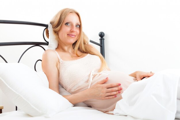 Blonde niedliche schwangere Frau auf weißem Kissen im Bett