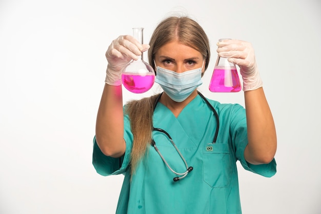 Blonde Ärztin, die Gesichtsmaske trägt und Chemikalien von einer Flasche zur anderen setzt