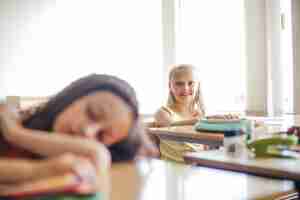 Kostenloses Foto blonde schulmädchen sitzen am tisch lächelnd