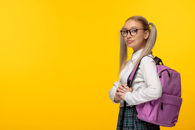 Blonde Studentin des Weltbuchtages mit Pferdeschwänzen und Brille auf gelbem Hintergrund