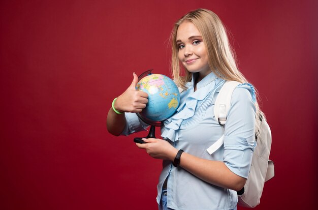 Blonde Studentin hält einen Globus und sieht positiv aus.