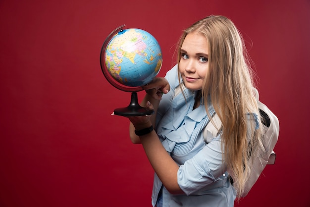 Blonde Studentin hält einen Globus und sieht positiv aus.