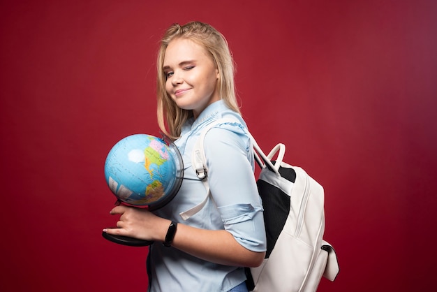 Blonde Studentin hält einen Globus und sieht positiv aus.