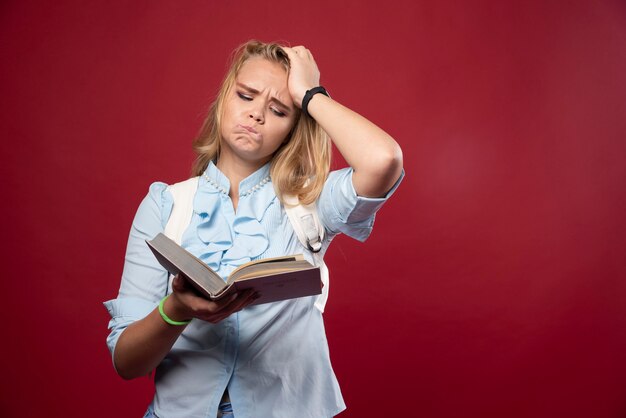 Blonde Studentin hält ihre Bücher und sieht erschrocken aus.