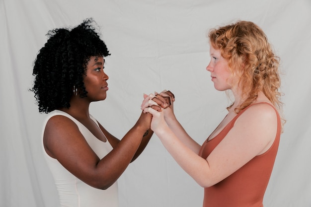 Blonde und afrikanische junge Frau, die vertraulich steht, Hände halten