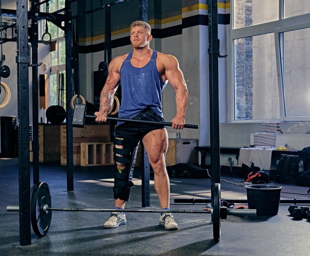 Blonder Bodybuilder mit gebrochenem Bein im Verband hält Cross-Fit-Hammer in einem Fitnessstudio.