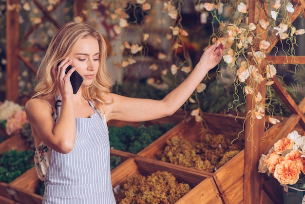 Blonder junger weiblicher Florist, der auf Mobiltelefon spricht