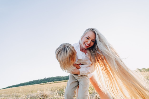 Blonder kleiner Junge, der mit Mutter mit weißen Haaren mit Heu im Feld spielt. Sommer, sonniges Wetter, Landwirtschaft. glückliche Kindheit.