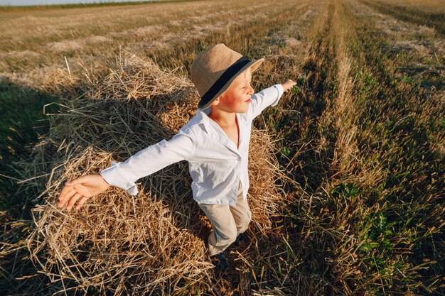 Blonder kleiner Junge, der Spaß hat, auf Heu im Feld zu springen. Sommer, sonniges Wetter, Landwirtschaft. glückliche Kindheit. Landschaft.