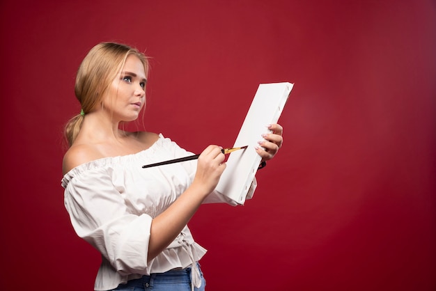 Blonder Kunstmeister, der mit einem Pinsel auf Leinwand arbeitet und überrascht die Person oder die Natur ansieht.