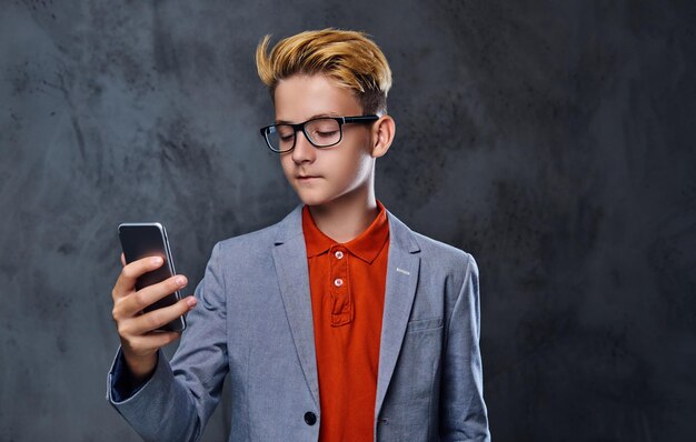 Blonder Teenager-Junge in Jacke und Brille hält Smartphone.