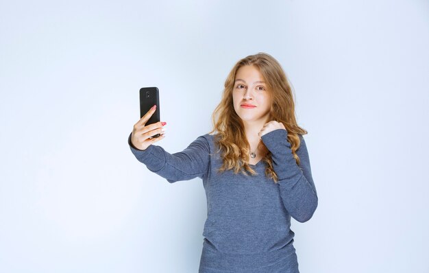 Blondes gelocktes Mädchen, das ihr selfie nimmt.