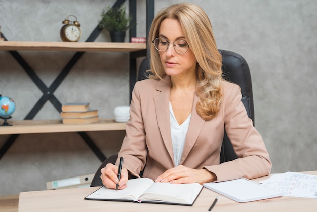 Blondes junges Geschäftsfrauschreiben auf Tagebuch mit Stift im Büro