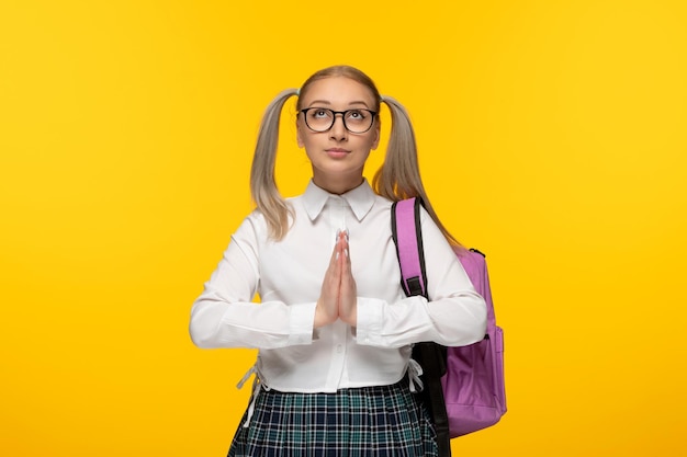 Blondes junges Mädchen des Weltbuchtages, das Hände zusammen auf gelbem Hintergrund betet