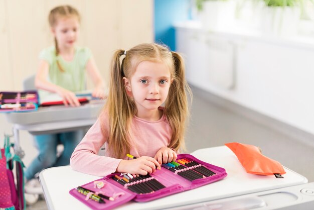 Blondes kleines Mädchen, das ein Federmäppchen auf ihrem Schreibtisch hat