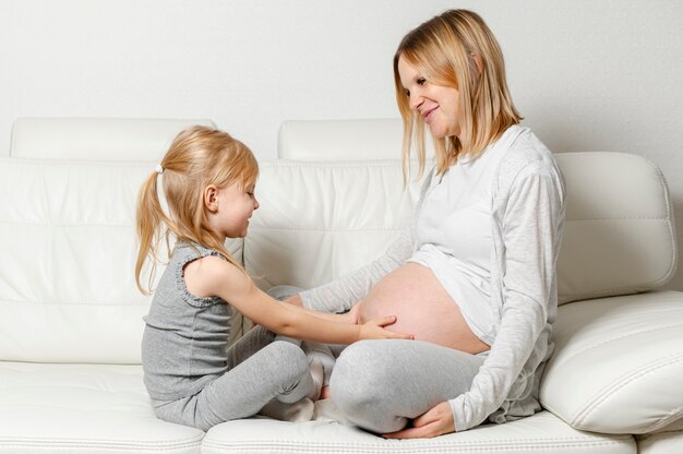 Blondes kleines Mädchen, das mit dem schwangeren Mutterbauch spielt