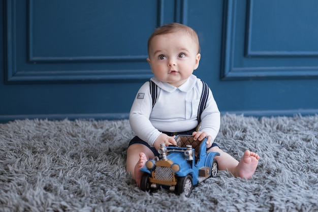 Blondes Kleinkind, das auf einem Teppich sitzt und mit einem blauen Auto spielt.