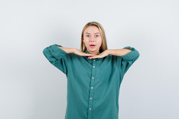 Blondes Mädchen, das die Hände unter dem Kinn in der grünen Bluse hält und hübsch aussieht.