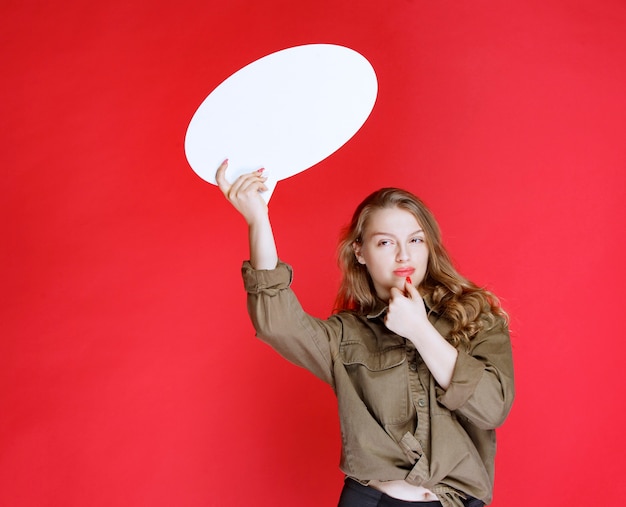 Blondes Mädchen, das ein weißes ovales Thinkboard hält und sich positiv fühlt.