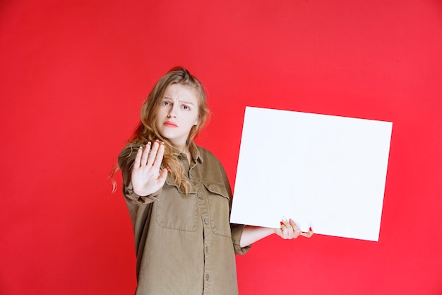 Blondes Mädchen, das eine Leinwand hält und unzufrieden aussieht.