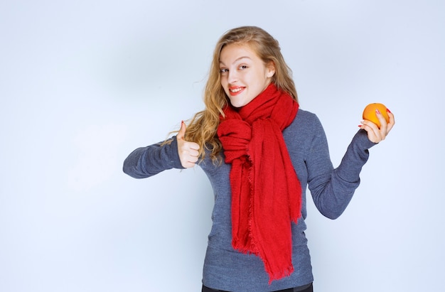 Blondes Mädchen, das eine orange Frucht hält und den Geschmack genießt.