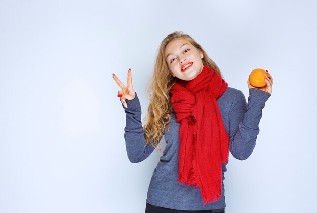 Blondes Mädchen, das eine orange Frucht hält und den Geschmack genießt.