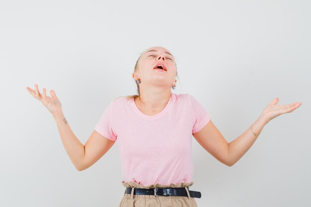 Blondes Mädchen, das Hände hebt, Kopf in T-Shirt, Hose zurückbeugt und friedlich, Vorderansicht schaut.