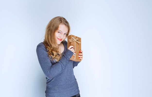 Blondes Mädchen, das ihre Pappgeschenkbox demonstriert und sich positiv fühlt.