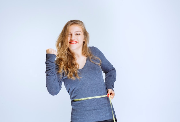 Blondes mädchen, das ihre taillengröße mit einem klebeband misst und sich erfolgreich fühlt.