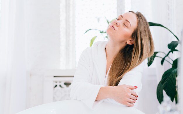 Blondes Mädchen, das im Badezimmer mit Bademantel aufwirft