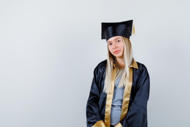 Blondes Mädchen, das in Absolventenuniform in die Kamera schaut und elegant aussieht