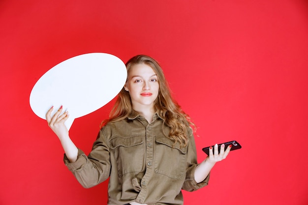 Blondes Mädchen, das in einer Hand ein ovales Ideaboard und in der anderen ein Smartphone hält.