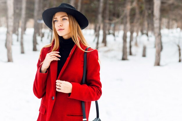 Blondes Mädchen, das roten Mantel auf einem schneebedeckten Feld trägt