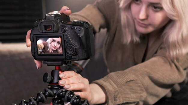 Blondes Mädchen des jungen Inhaltsschöpfers, das eine Kamera auf ein Stativ setzt und sich filmt, wie sie für vlog spricht