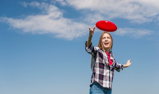 Blondes Mädchen des niedrigen Winkels, das einen roten Frisbee wirft