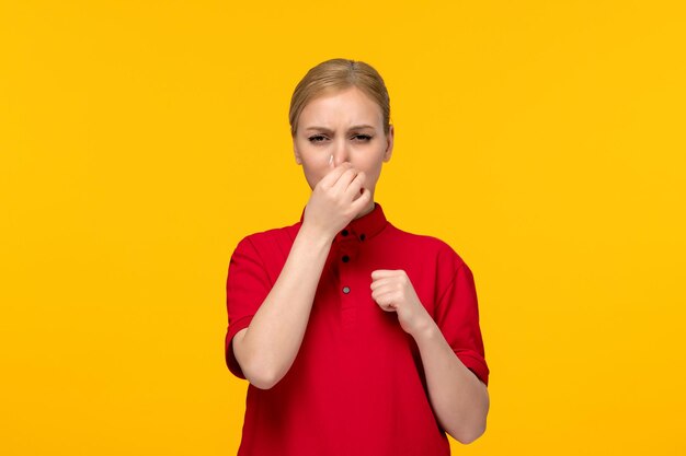 Blondes Mädchen des roten Hemdtages, das ihre Nase in einem roten Hemd auf einem gelben Hintergrund bedeckt