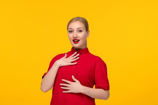 Blondes Mädchen des roten Hemdtages überraschte in einem roten Hemd und in einem Lippenstift auf einem gelben Hintergrund