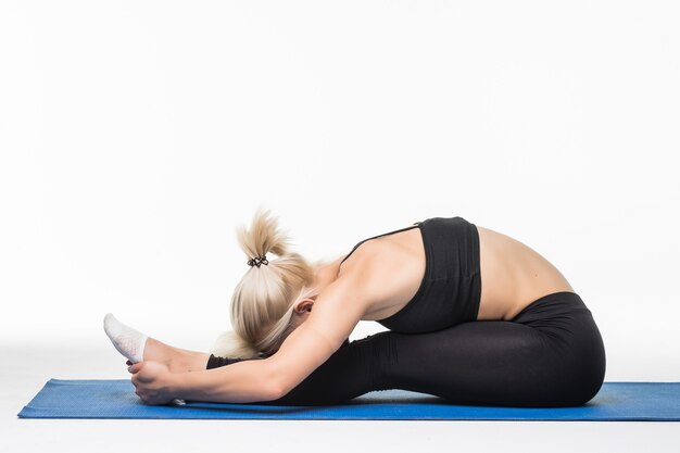 Blondes Mädchen haben eine entspannende Yoga-Zeit nach Sportübungen auf dem Boden, die auf einer Sportkarte sitzen