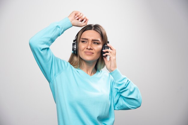 Blondes Mädchen im blauen Sweatshirt, das Kopfhörer trägt, die Musik genießt und Spaß hat.