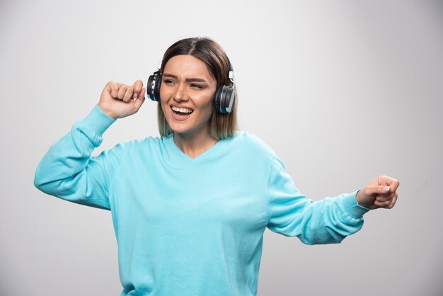 Blondes Mädchen im blauen Sweatshirt, das Kopfhörer trägt, die Musik genießt und Spaß hat