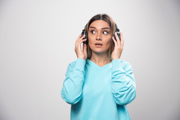Blondes Mädchen im blauen Sweatshirt, das Kopfhörer trägt und versucht, die Musik zu verstehen.
