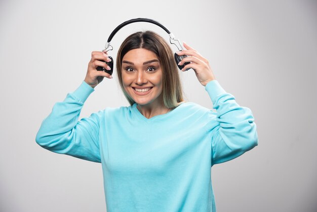 Blondes Mädchen im blauen Sweatshirt hält Kopfhörer und macht sich bereit, sie zu tragen, um die Musik zu hören.