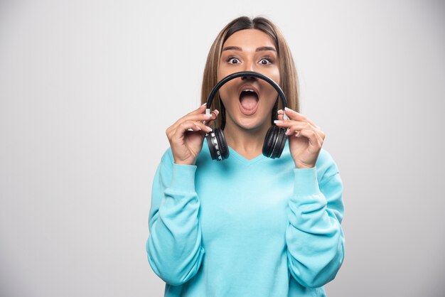 Blondes Mädchen im blauen Sweatshirt hält Kopfhörer und macht sich bereit, sie zu tragen, um die Musik zu hören.