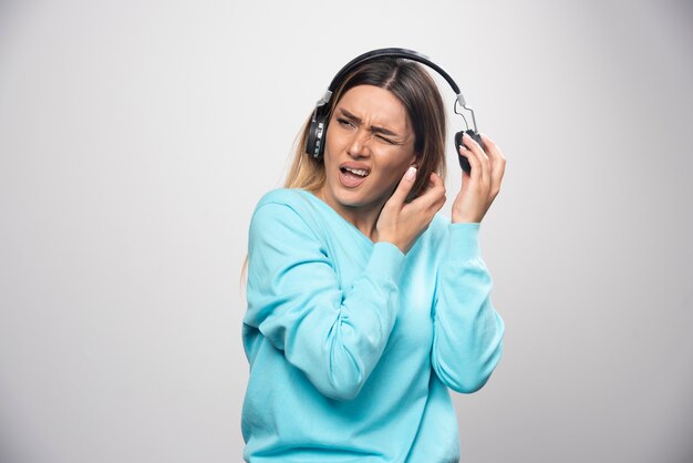 Blondes Mädchen im blauen Sweatshirt hört die Kopfhörer und genießt die Musik nicht.