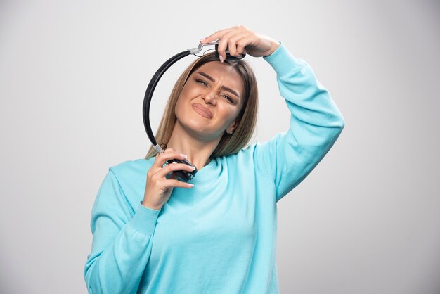 Blondes Mädchen im blauen Sweatshirt hört die Kopfhörer und genießt die Musik nicht.