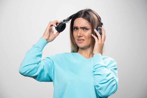 Blondes Mädchen im blauen Sweatshirt hört die Kopfhörer und genießt die Musik nicht.