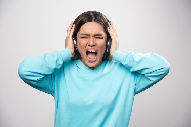 Blondes Mädchen im blauen Sweatshirt hört die Kopfhörer und genießt die Musik nicht